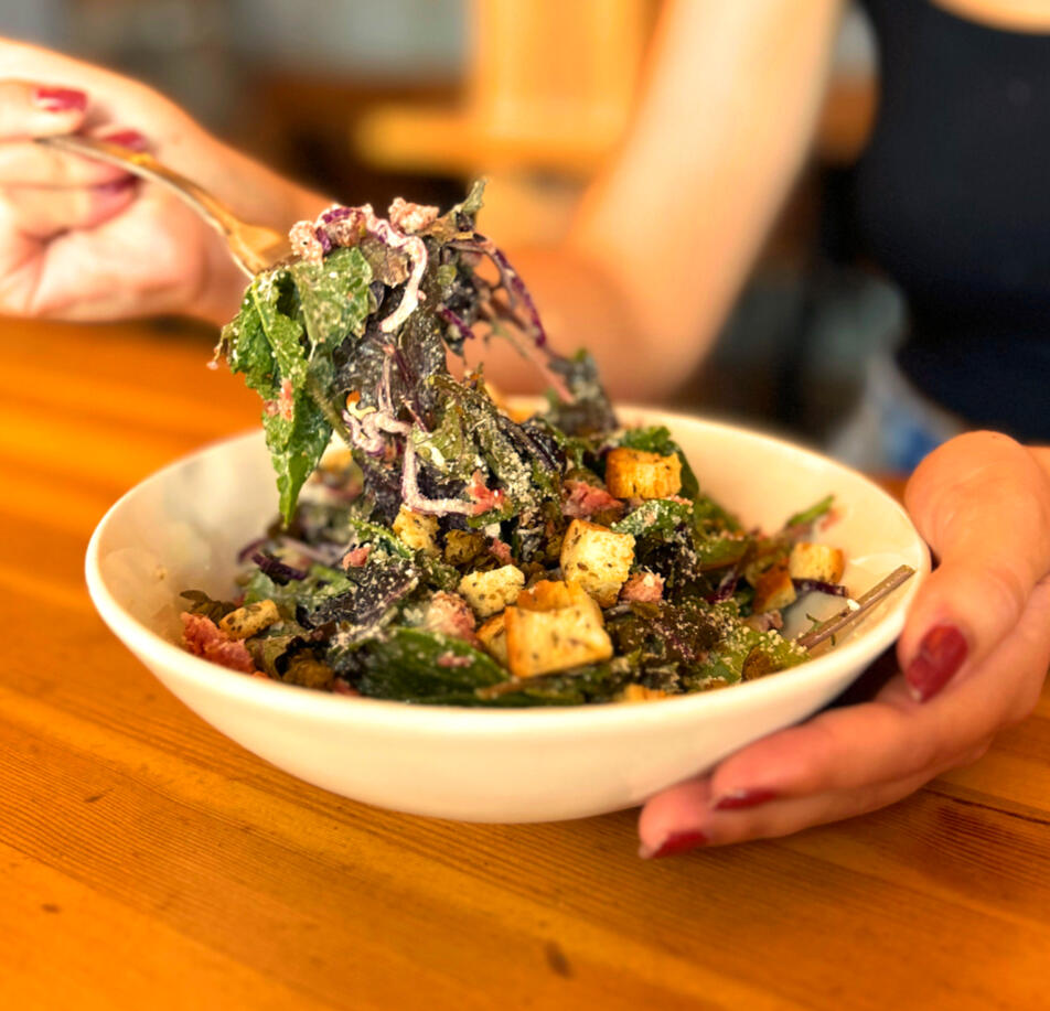 Kale caesar salad with mixed baby kales, julienne red cabbage, roasted local bacon bits, grated parmesan, house made caesar dressing, crispy capers and croutons, served at Swans Pub in Victoria, BC